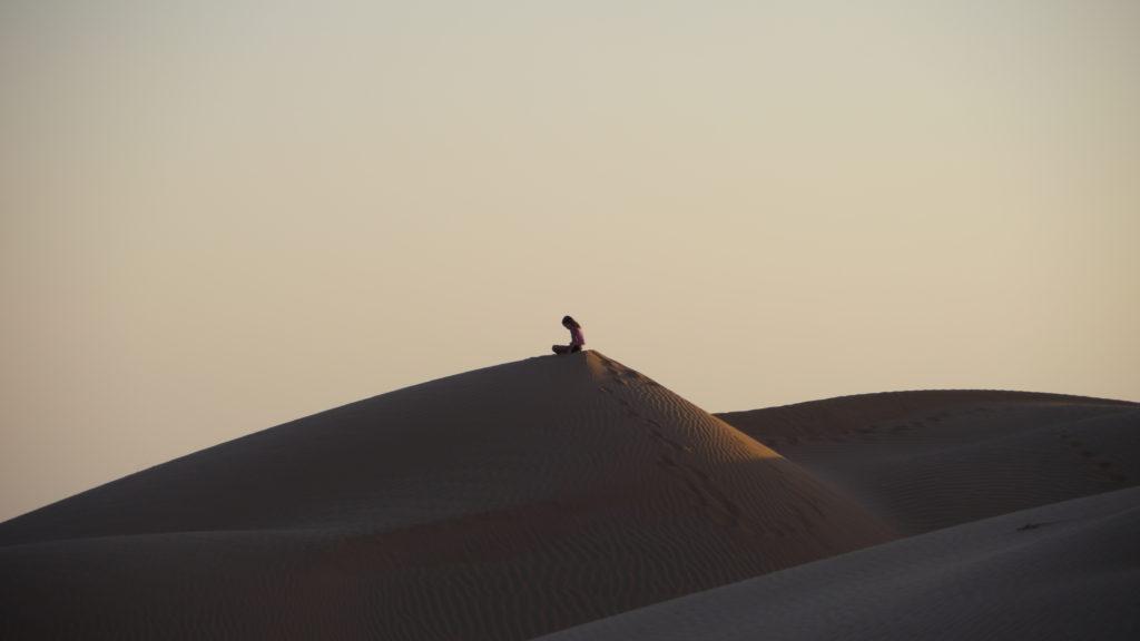 Child on a sand dune of Empty Quarter in Oman. Sunset in the desert trip from Salalah.
